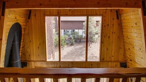 Une cabane en bois avec une grande fenêtre, un banc en bois et un arbre à l’extérieur.