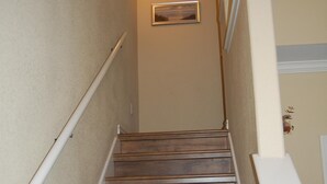 Una escalera de madera con barandillas blancas, paredes color beige y decoración en las paredes.