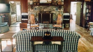 Un salon chaleureux avec une cheminée en pierre, deux fauteuils, un canapé et un téléviseur.