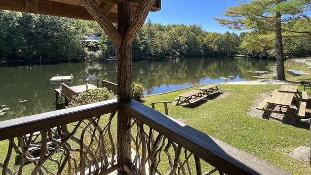 Une terrasse en bois surplombant un lac paisible, où sont amarrés des bateaux, et où l'on trouve des tables de pique-nique et une végétation luxuriante.