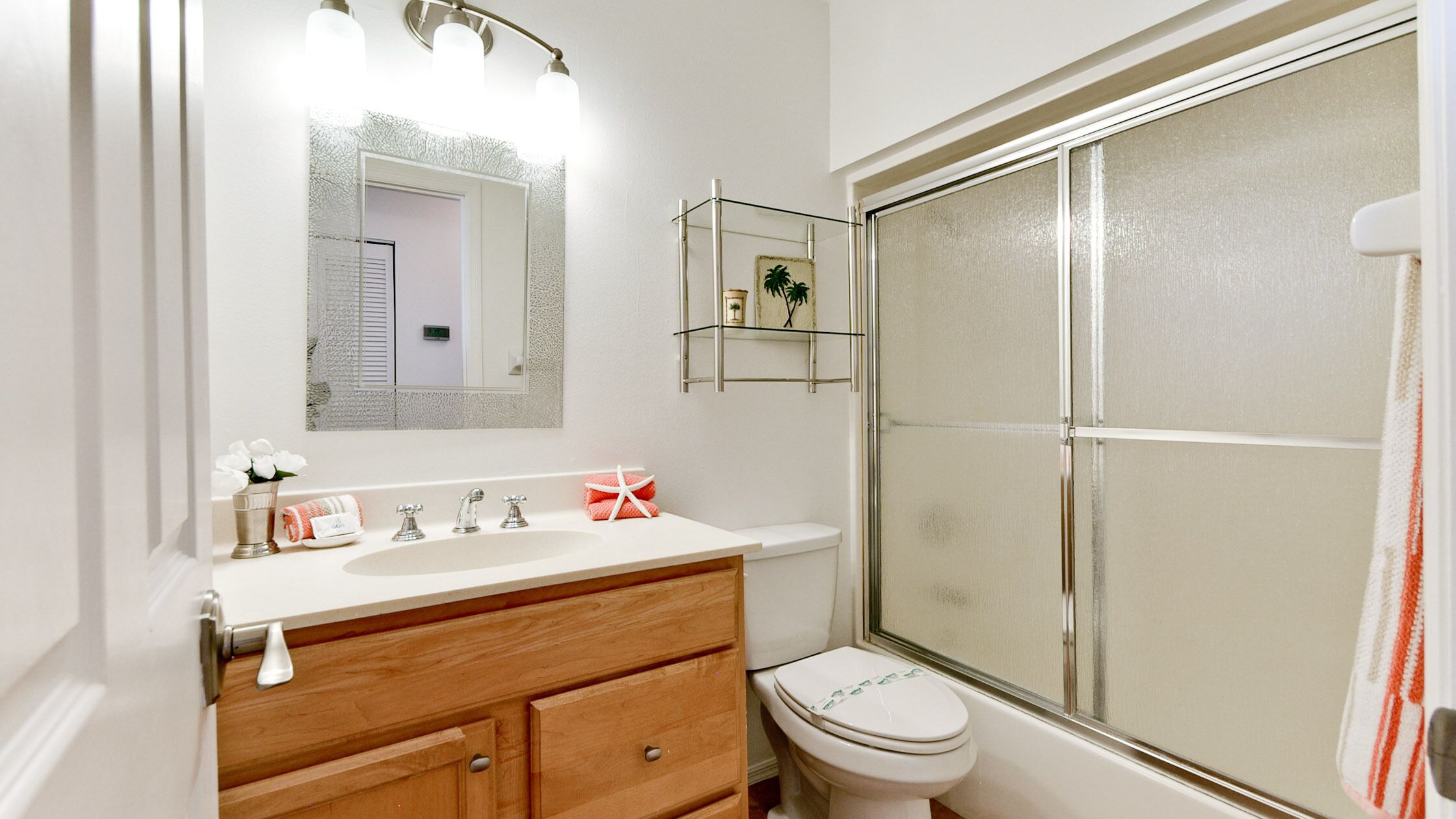 Un bagno con un lavandino bianco, una cassettiera in legno, un box doccia in vetro e un water.