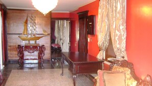 A room with a wooden table, a patterned sofa, a chandelier, and a red wall. - Room #6 We are only 30 min. away from  "BASEBALL HALL OF FAME" in Coopers Town . (Fort Plain)