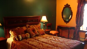 A bed with a patterned bedspread, a wooden headboard, and multiple pillows. There is a nightstand with a lamp, a chair, and a mirror on the wall. - Room #6 We are only 30 min. away from  "BASEBALL HALL OF FAME" in Coopers Town . (Fort Plain)