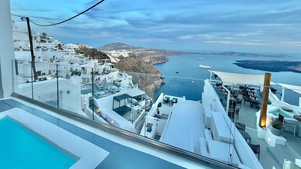 Un hotel moderno con piscina y terraza en la azotea, con vistas a un paisaje costero de edificios blancos y al mar.