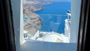 Vista a través de una ventana de un edificio con vistas a un paisaje costero, con un mar azul cristalino y terreno rocoso.