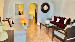 Una sala de estar acogedora con sofá, sillón y mesa de centro, un arco que da a otra habitación y un espejo redondo en la pared.