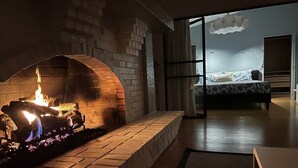 Un salon moderne avec une cheminée en briques, un lit recouvert d’une couvre-lit à motifs floraux et une grande fenêtre donnant sur le ciel.