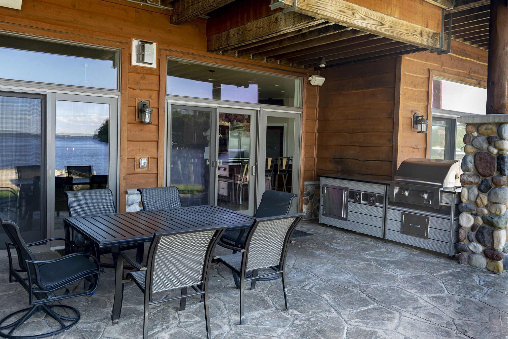 An outdoor patio with a stone table and chairs, a grill, and a stone wall.