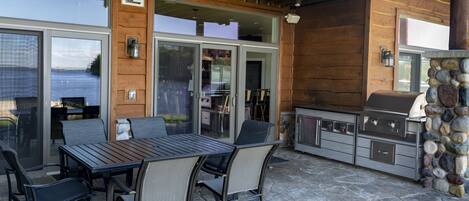 An outdoor patio with a stone table and chairs, a grill, and a stone wall.