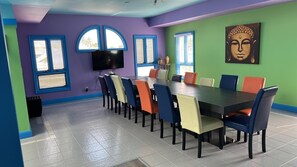 A dining area with a long table and colorful chairs, a flat-screen TV mounted on the wall, and a Buddha painting on the green wall. - Real World MTV House-18 to 22 guests, Not Just a  House Your Own Private Resort (Key West)