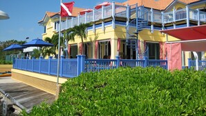 Ein Hotel mit blauer und gelber Fassade, einer Fahnenstange mit der Flagge der Cook Islands und einem Balkon mit blauer Geländer.
