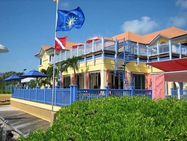 A hotel with a blue and yellow facade, a flagpole with the flag of the Cook Islands, and a balcony with a blue railing. - Real World MTV House-18 to 22 guests, Not Just a  House Your Own Private Resort (Key West)