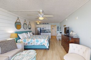 A compact room with a bed, a small sofa, a round coffee table, a dresser, and a television.