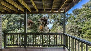 Una terraza de madera con barandilla metálica que da a un jardín con diversas plantas y árboles.