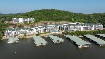 A large resort with multiple buildings, a dock area with boats, and a backdrop of a forested hill.