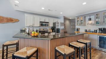 A modern kitchen with a central island, bar stools, and a coffee bar.