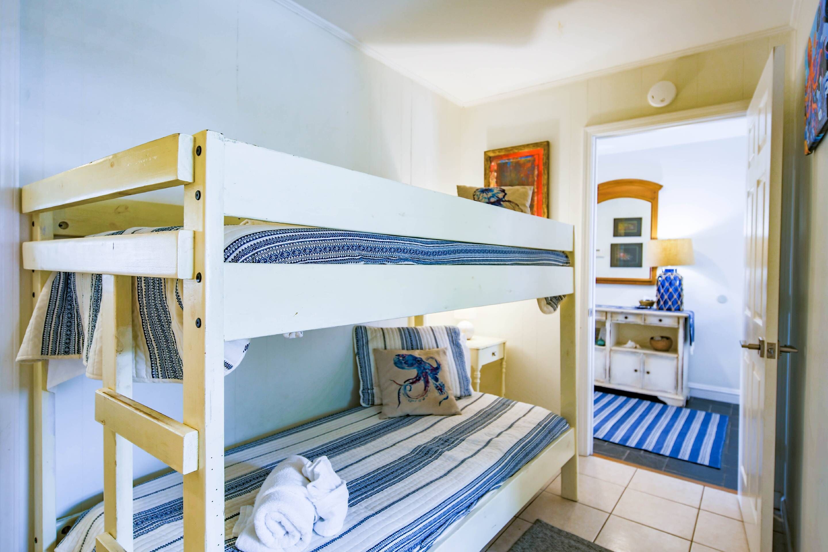 A bunk bed room with striped bedding, a pillow with a dragon design, and a small bedside table with a lamp.