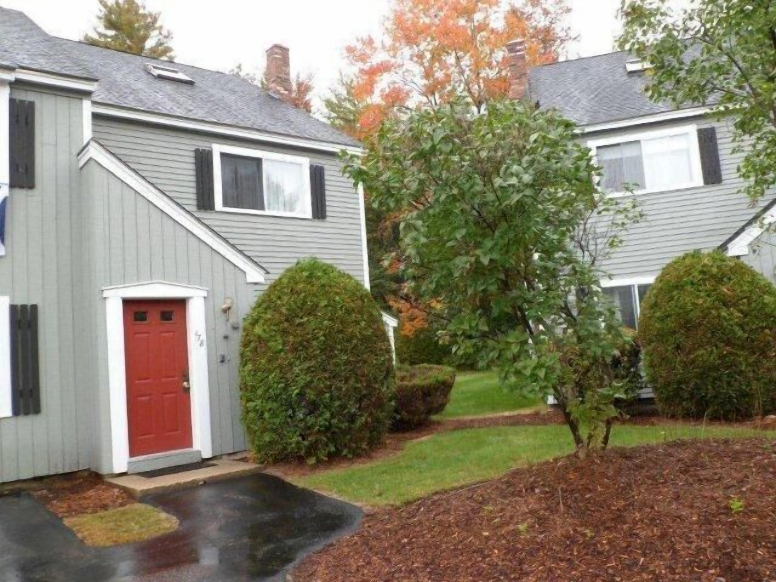 A residential building with a red door, two well-maintained hedges, and a grassy lawn.