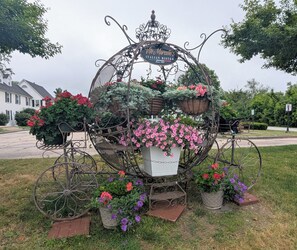 Un chariot en fer forgé, orné d’une enseigne indiquant le nom du restaurant italien de Vito Marcelli, est entouré de plantes et de fleurs en pot.