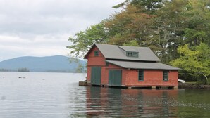 Ein rotes, aus Holz gebautes Hausboot auf einem ruhigen See vor einer Bergkulisse.