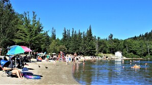 Ein Strand am Seeufer mit badenden und sonnenden Personen, umgeben von dichtem Wald.