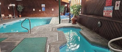An indoor swimming pool with a wooden interior, a lifeguard warning sign, and lounge chairs.