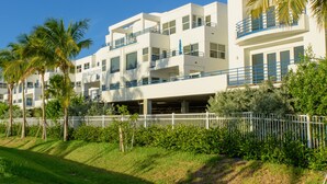 A modern multi-story hotel with balconies, a covered parking area, and lush greenery.