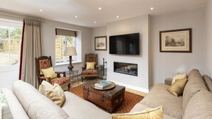 Una sala de estar con un sofá, una mesa de centro de madera con libros, una maleta antigua, un televisor y cuadros en la pared.