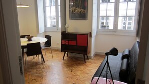 A room with a wooden herringbone floor, a round dining table with chairs, a black sofa, a red and black cabinet, and a poster on the wall. - House of the Cathedral - 2 bedroom apartment near the Cathedral (historic center) (Porto)