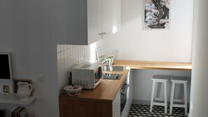 A kitchen with white cabinets, a microwave, a sink, and a wooden countertop. There are two white stools and a framed picture on the wall. - House of the Cathedral - 2 bedroom apartment near the Cathedral (historic center) (Porto)
