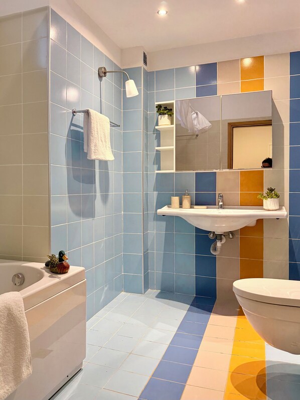 Un baño con bañera, lavamanos e inodoro, con azulejos azules y amarillos.