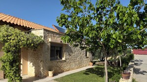 Una casa de piedra con techo de tejas, una ventana pequeña y un jardín con césped y plantas en macetas.