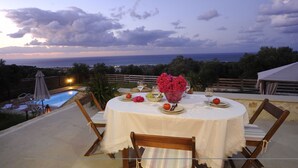 Un área de comedor al aire libre con una mesa preparada para dos personas, con vista a una piscina y un paisaje pintoresco.