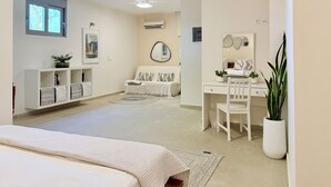 Un dormitorio con cama, escritorio, silla, espejo y una planta en maceta.