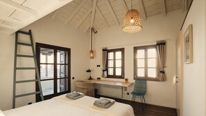 Een slaapkamer met een bed, bureau, stoel, ladder en grote ramen.