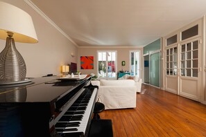 Um quarto com um piano, uma cama, um abajur e um quadro abstrato colorido na parede.