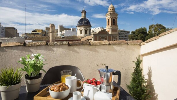 A breakfast tray with croissants, coffee, and fruit on a terrace with a view of a church and cityscape. - Botanico Atico Duplex 302 (Valencia ciudad)
