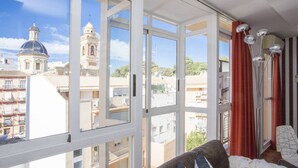 A room with large windows, a sofa, and a view of a church and buildings. - Botanico Atico Duplex 302 (Valencia ciudad)
