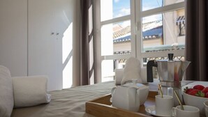 A neatly made bed with a wooden tray, white cups, a coffee pot, and a bowl of strawberries on a table by a window with a view of buildings. - Botanico Atico Duplex 302 (Valencia ciudad)