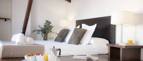 A hotel room with a neatly made bed, bedside lamps, a tray with breakfast items, and a small table with a book and a glass of orange juice.