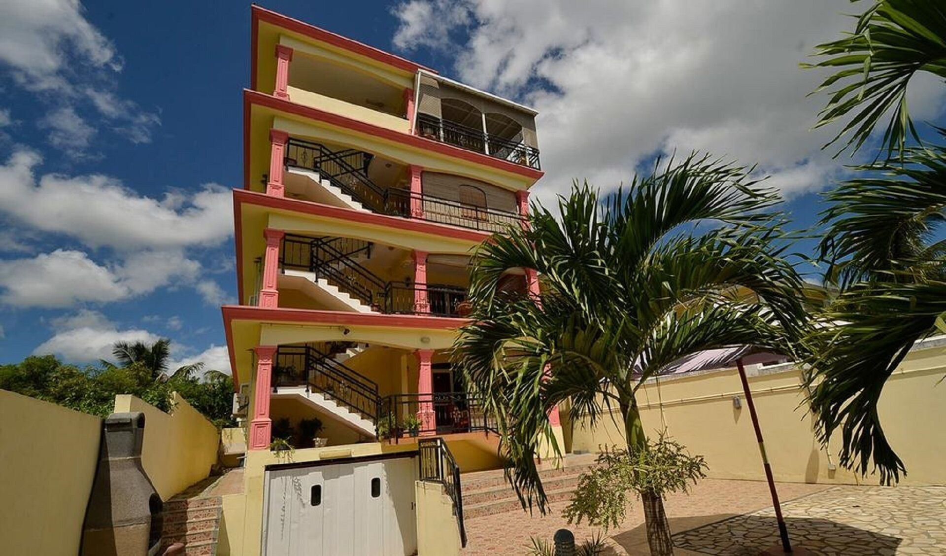 A multi-story building with balconies, a staircase, and a palm tree in the foreground.