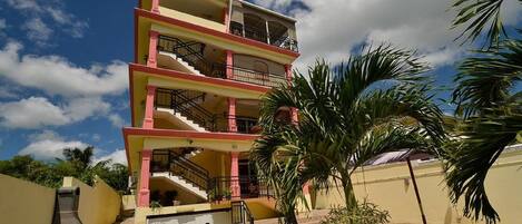 A multi-story building with balconies, a staircase, and a palm tree in the foreground.