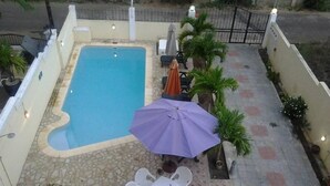 Ein Pool mit Steinrand, umgeben von einer mit Fliesen ausgelegten Terrasse mit Tisch und Stühlen.