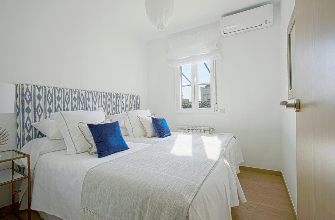 Un dormitorio con cama, mesitas de noche y una ventana.