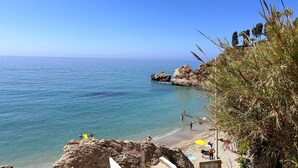 A beach with clear blue water, rocky outcrops, and people swimming.