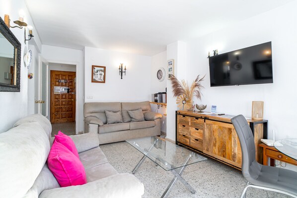 A living room with a sofa, a glass coffee table, a wooden cabinet, and a TV mounted on the wall.