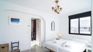 A bedroom with a bed, a chair, a small table, a mirror, and a window.