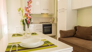 A modern kitchen with white cabinets, a dining table set with plates, cutlery, and a vase of flowers. - Casa Failla Taormina center (Taormina)