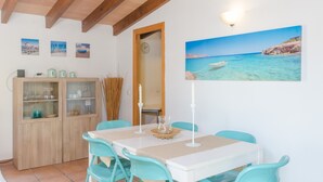 A dining area with a white table, turquoise chairs, and a wooden cabinet with glass doors.