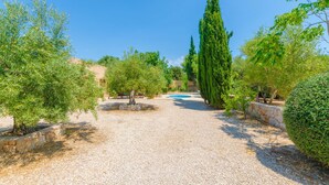 A gravel pathway leading to a pool surrounded by trees and stone walls.